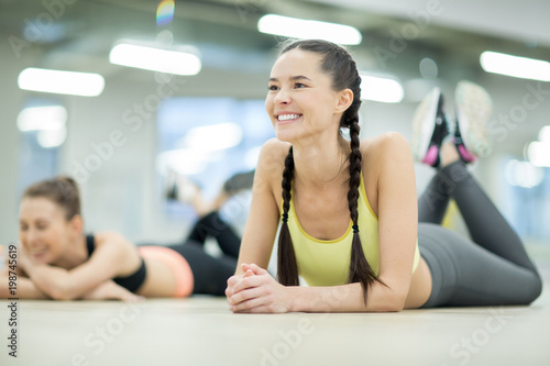 Happy girl with toothy smile lying on her belly and listening to trainer instructions during workout in sports center