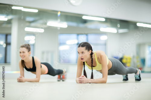 Exhausted young woman going on doing planks while looking at her trainer during workout