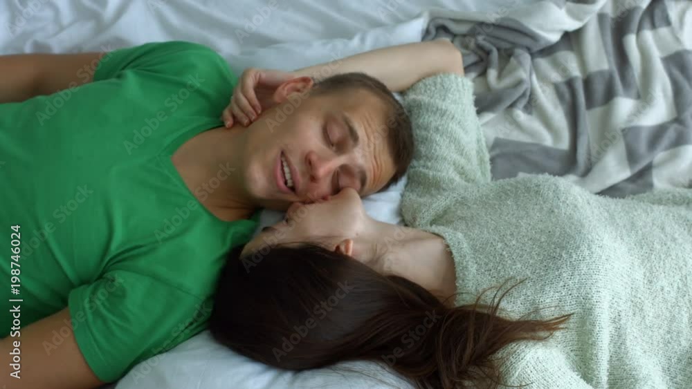 Portrait of romantic couple in love lying on bed face to face and bonding while spending leisure together at home. Top view. Affectionate couple chatting while lying on bed in opposite direction. Portrait of romantic couple in love lying on bed face to face and bonding while spending leisure together at home. Top view. Affectionate couple chatting while lying on bed in opposite direction.