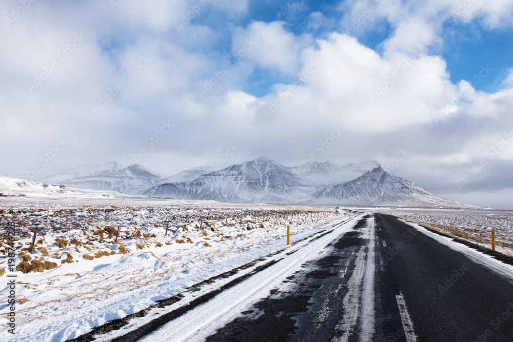 beautiful Iceland road heading to snow capped mountain with nice sky and cloud in sunny in winter.