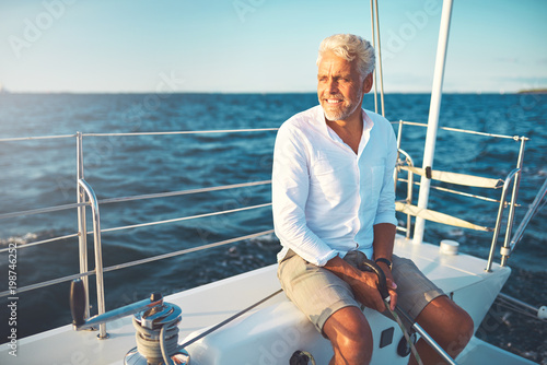 Fotografiet Smiling mature man sailing his yacht on a sunny day