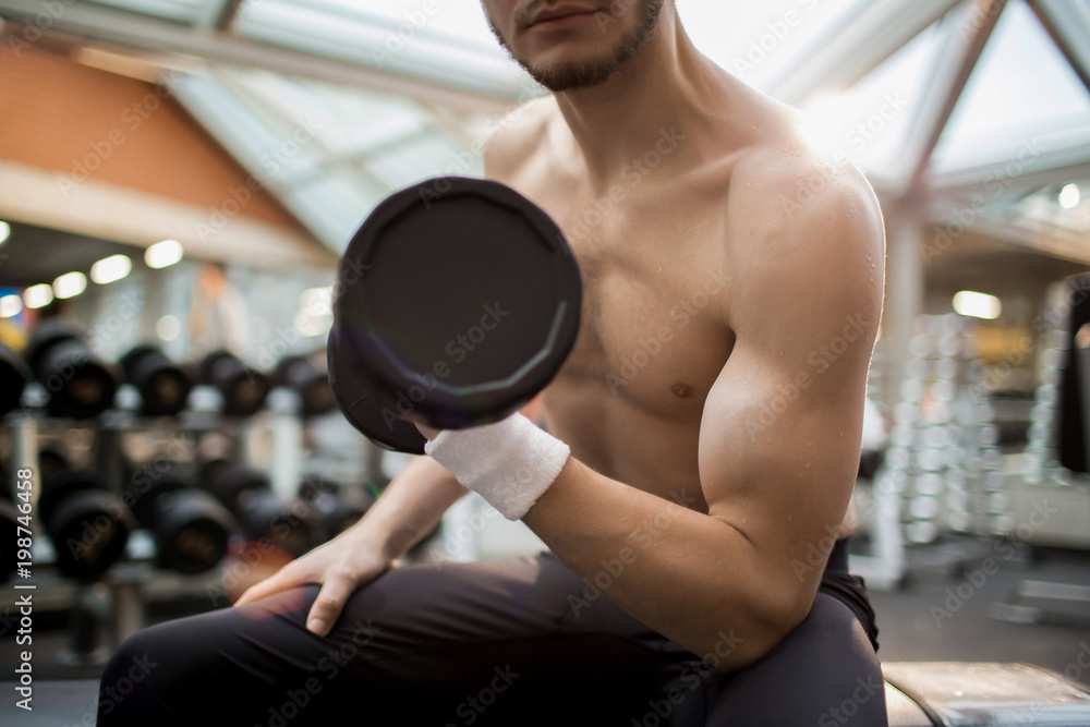 Fototapeta premium Muscular young man exercising with heavy barbell in one hand while training in sports center