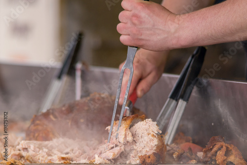 man carving pork joint with fork and knife at hog roast