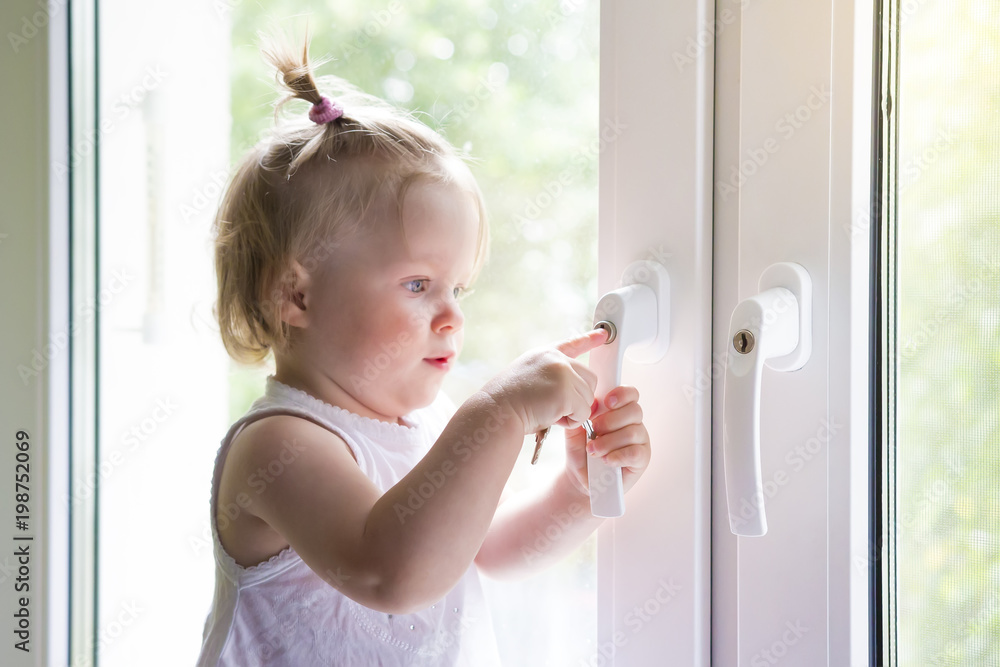 Child opens window with lock. Protection from falling out of child from window. little girl is standing on windowsill. child plays with keys at the window.