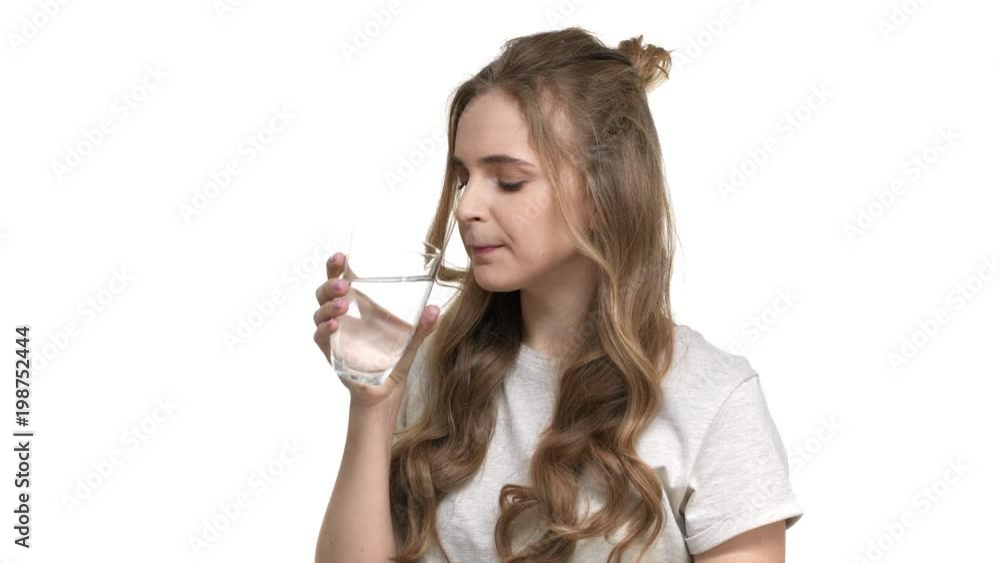 Portrait of good-looking woman with brown curly hair being dehydrated and drinking mineral water from transparent glass, over white background closeup. Concept of emotions Portrait of good-looking woman with brown curly hair being dehydrated and drinking mineral water from transparent glass, over white background closeup. Concept of emotions