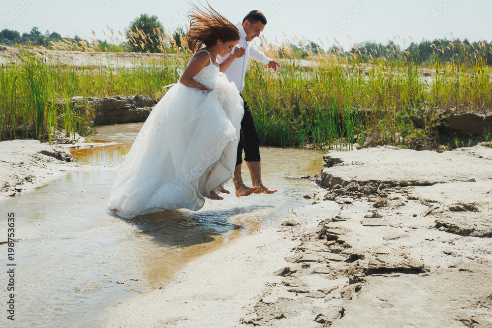 Wedding couple is running and jumping over the river beach with