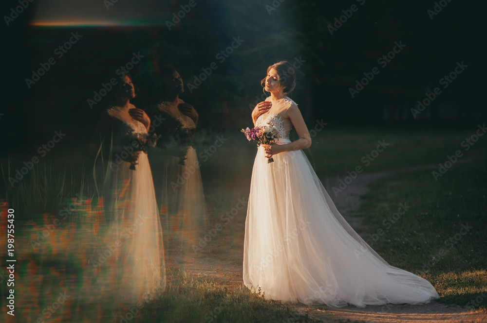 Young woman in a white dress is standing on the field. Portrait of girl outdoor. Romantic young woman posing on the background of sunset sky.