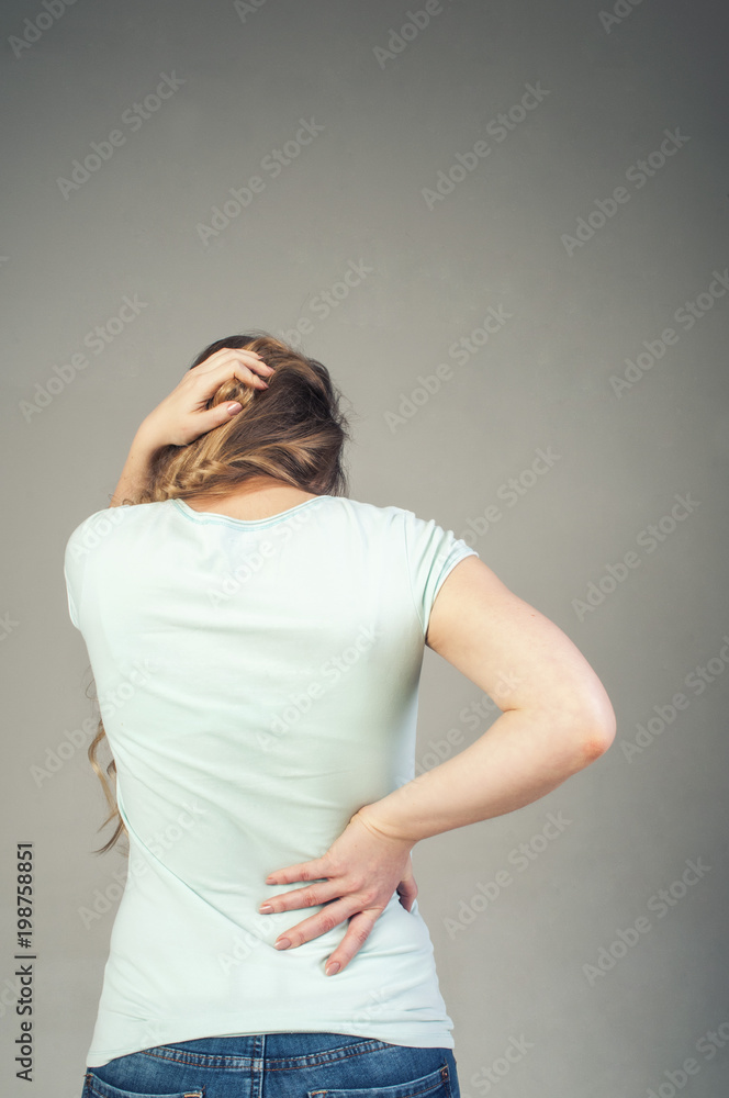 A young girl from the back with a strong headache and back pain. Convulsive spasm and headaches concept. Woman with back pain holding her aching back - body pain A young girl from the back with a strong headache and back pain. Convulsive spasm and headaches concept. Woman with back pain holding her aching back - body pain