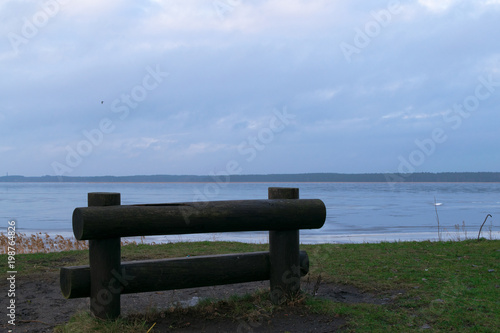 old wooden bench on the grass with view of the water and sky photo