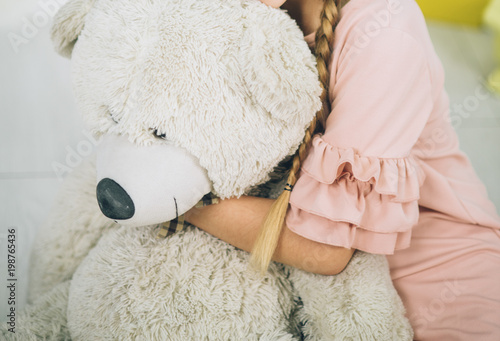 cute girl is hugging bear toy in the dress sitting