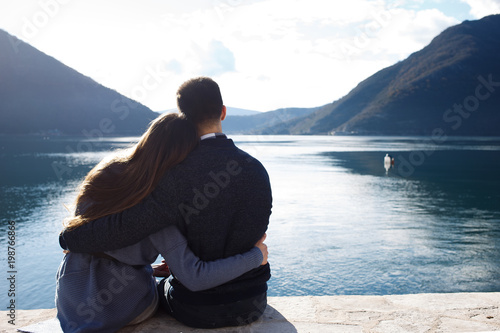 couple hugging and watching the sea sitting on the e beach