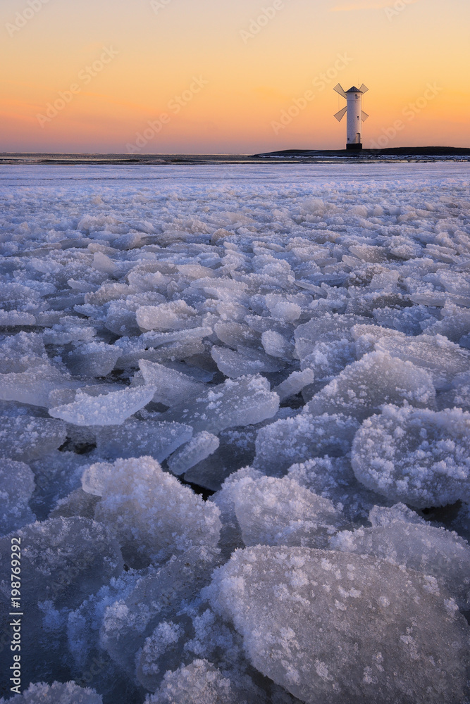 Fototapeta premium Beautiful sunrise over a windmill-shaped lighthouse. Swinoujscie, Poland.