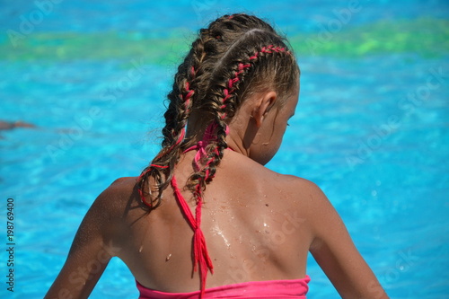 Young girl with braided hair sitting near pool