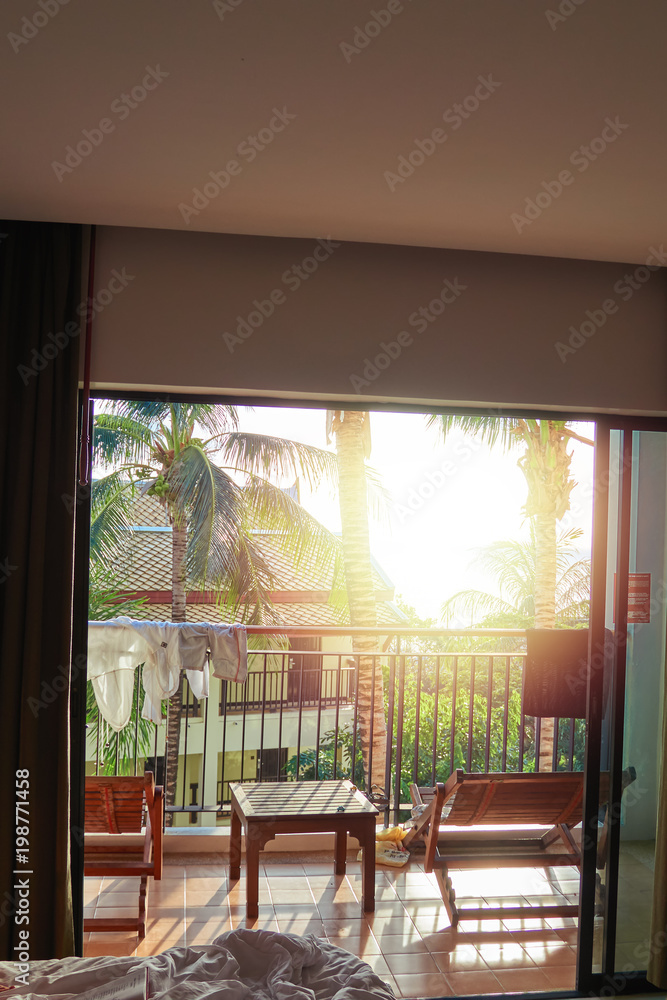 Beautiful evening sunshine shines in hotel room. Concept rest, travel. Tropical resort bedroom, palm trees, balcony with sun loungers and sliding glass doors. Beautiful evening sunshine shines in hotel room. Concept rest, travel. Tropical resort bedroom, palm trees, balcony with sun loungers and sliding glass doors.