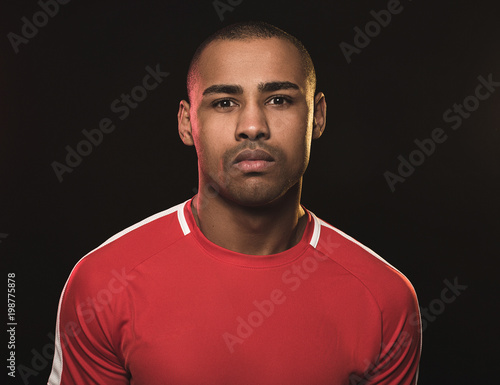 portrait of handsome African guy in red T-shirt. He looking calm and cold but defiantly. Isolated on black background