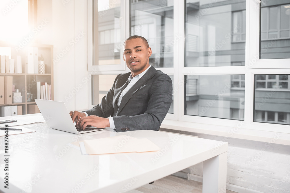 Waist up portrait of african man sitting at office and dialing text on computer. He looking confident with smile at camera. Copy space in right side Waist up portrait of african man sitting at office and dialing text on computer. He looking confident with smile at camera. Copy space in right side