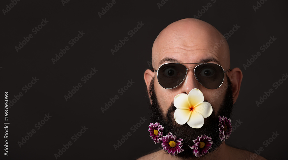 unshaven man with beard with flowers and sunglasses on dark background with copyspace