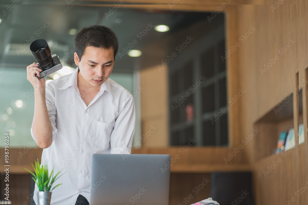 Young man holding a camera and using laptop. Young man holding a camera and using laptop.