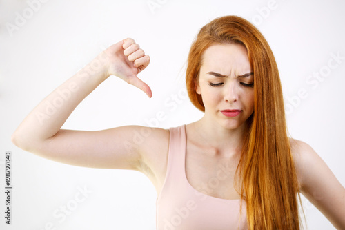 Image of young redhead lady showing thumbs down. Looking camera. frustrated face. negative emotions