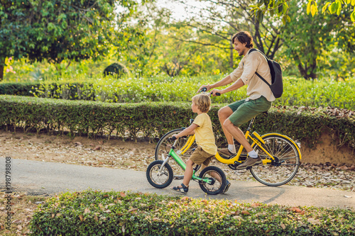 Happy family is riding bikes outdoors and smiling. Father on a bike and son on a balancebike photo