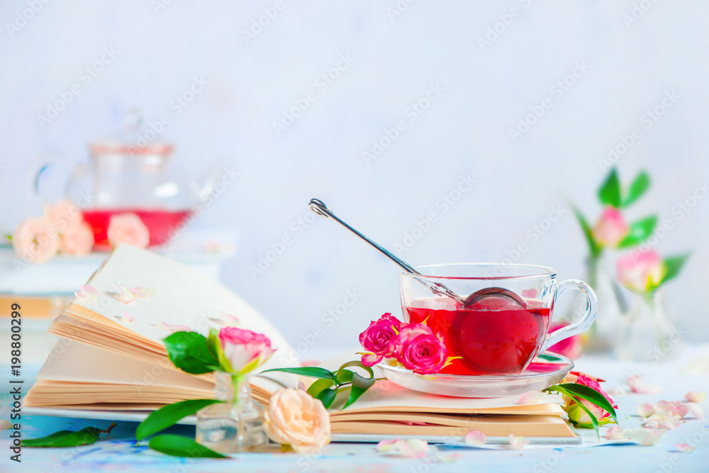 Cup of rose petals tea on an open book on a white background with spring flowers. Romantic still life with copy space. Leisure and reading concept. Cup of rose petals tea on an open book on a white background with spring flowers. Romantic still life with copy space. Leisure and reading concept.