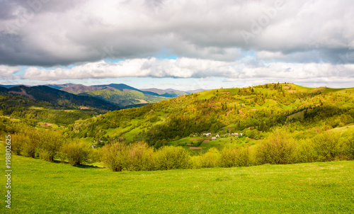 lovely rural scenery in mountains. grassy meadows under the cloudy sky on a bright day. village on a hillside in the distance