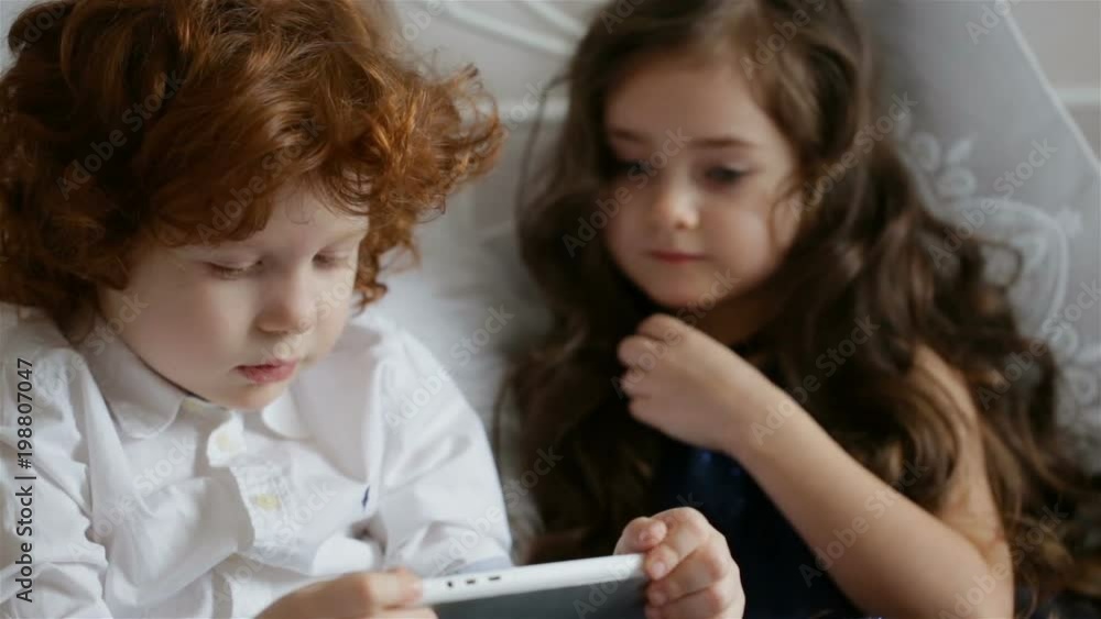 A boy and a girl lie on the bed and try to turn on the tablet computer A boy and a girl lie on the bed and try to turn on the tablet computer