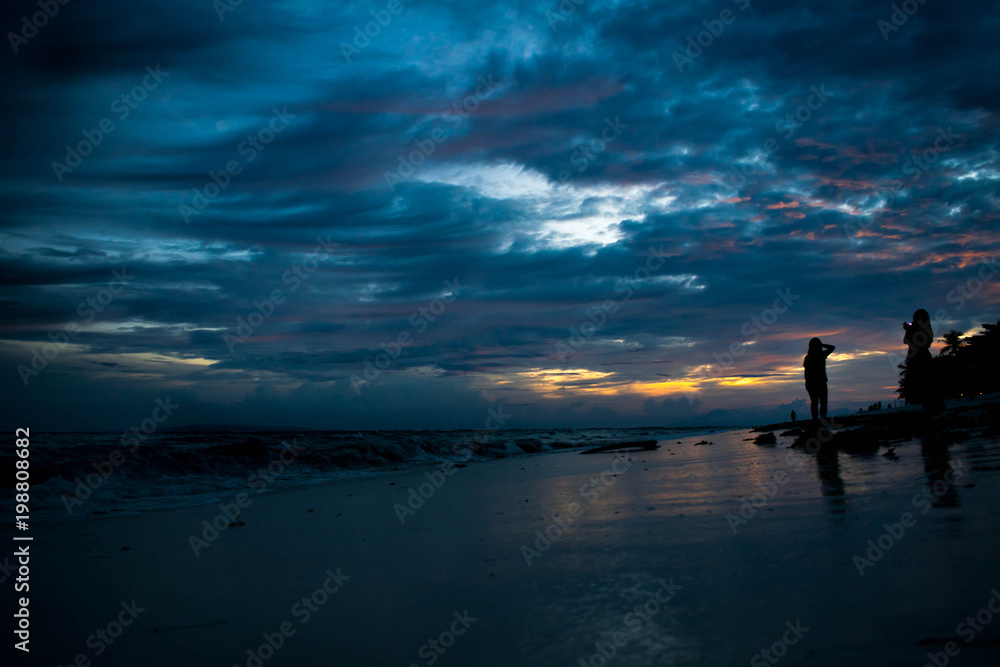 The beach during a blue hour with silhouette of young women at the side enjoying the beach