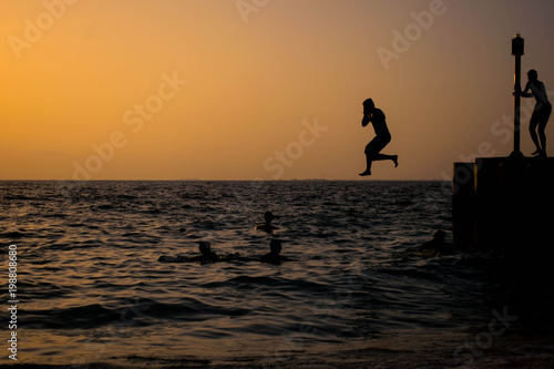 A young man jumping from a pier at the beach during sunset