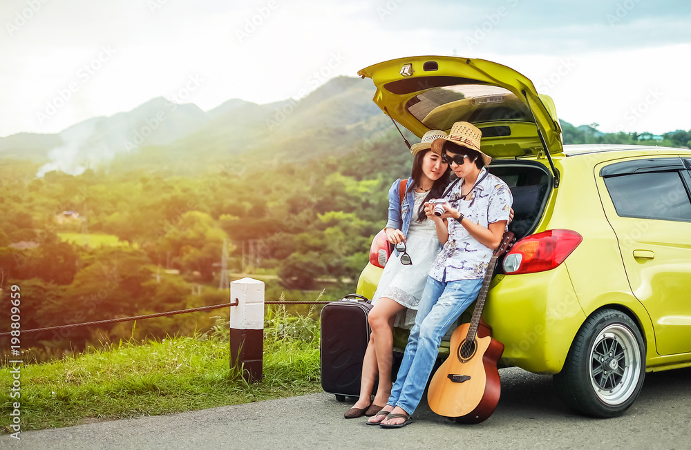 Couple of traveler sitting on hatchback of car and looking at the picture on camera. tourist couple have a good time on vacation. Couple of traveler sitting on hatchback of car and looking at the picture on camera. tourist couple have a good time on vacation.