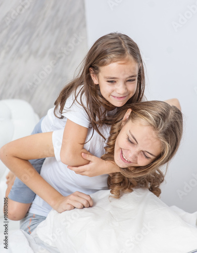 Happy family - mother and daughter have fun on the bed