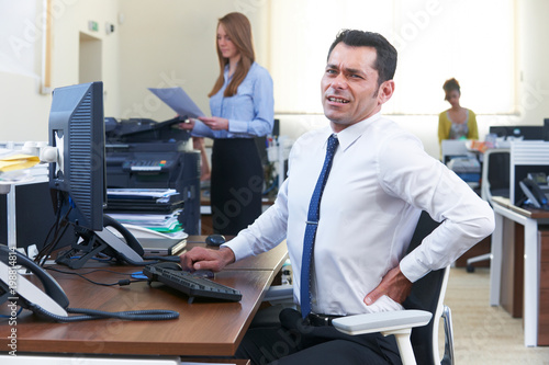 Businessman Working At Desk Suffering From Backache
