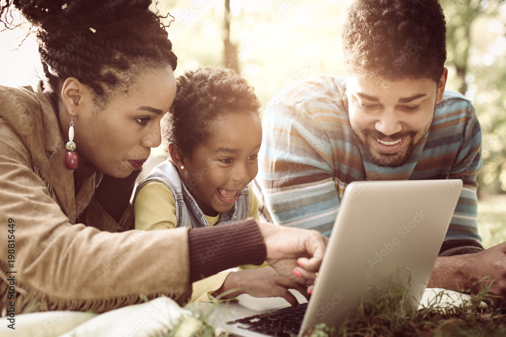 Cheerful African American family lying down in park and using laptop. Cheerful African American family lying down in park and using laptop.