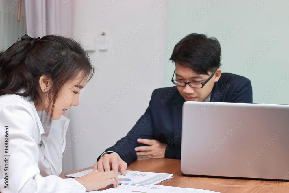 Two young Asian business people analyzing paper work or charts together in modern office. Team work business concept. Selective focus and shallow depth of field. Two young Asian business people analyzing paper work or charts together in modern office. Team work business concept. Selective focus and shallow depth of field.