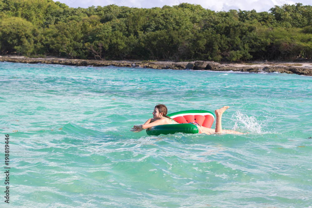 Beautiful teenage girl having fun at the beach with an inflatable toy in the Caribbean sea. Freedom or vacations concept