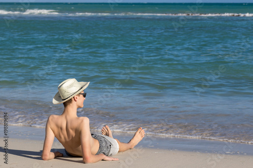 Teenage boy relaxing at the sea shore on sandy beach and enjoying view to the open sea