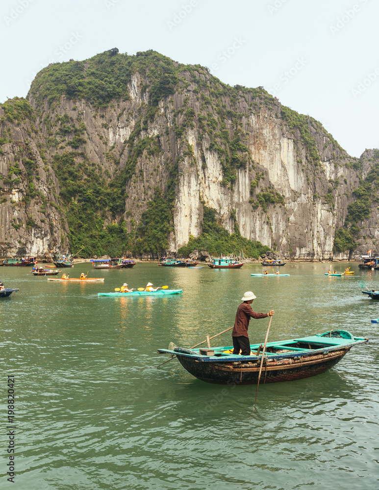 Man rowing boat over emerald water with limestone island in background in summer at Quang Ninh, Vietnam.
