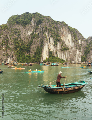 Man rowing boat over emerald water with limestone island in background in summer at Quang Ninh, Vietnam. © artitwpd