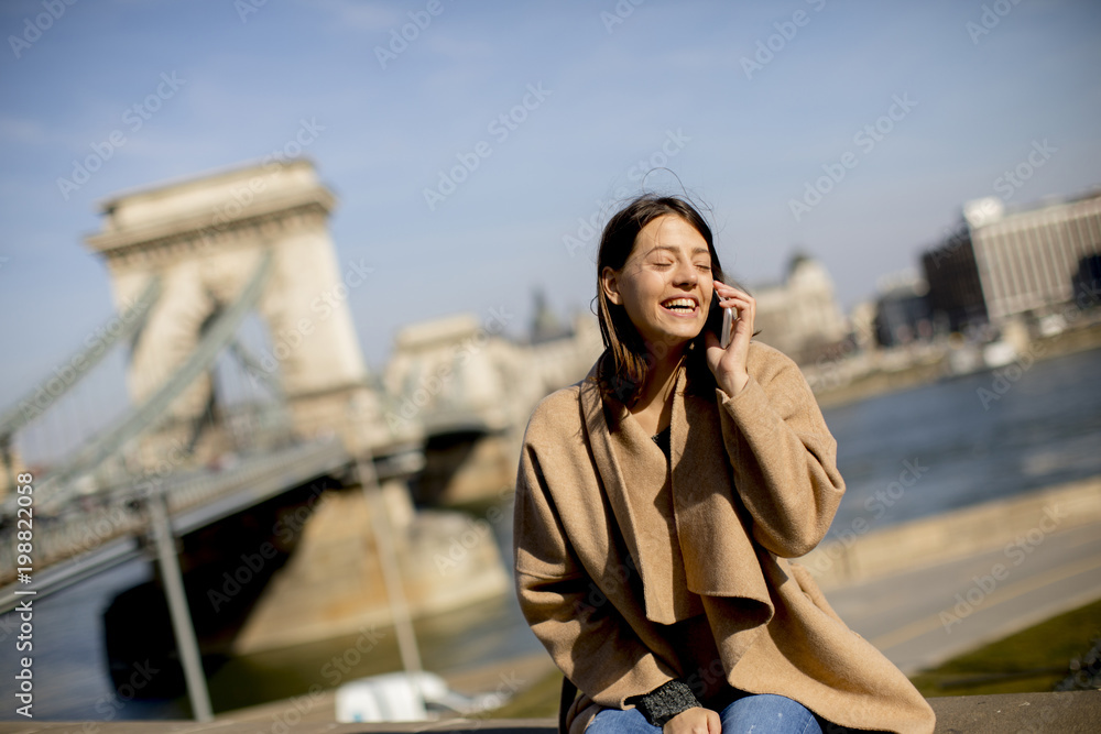 Fototapeta premium Young woman using mobile phone with Chain bridge at background in Budapest