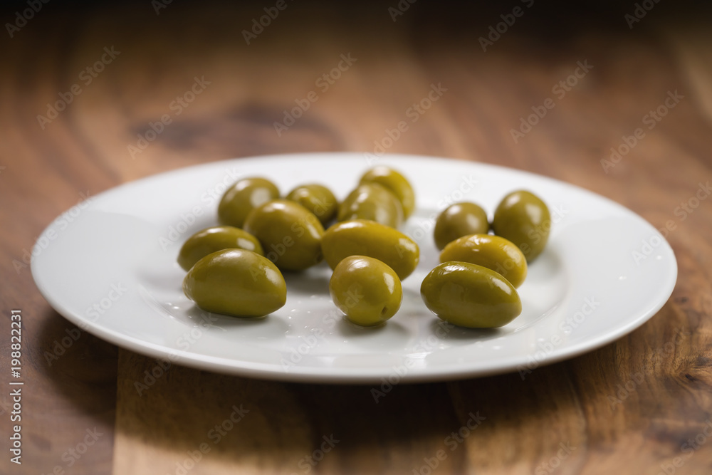 big green salted olives on white plate on wooden table big green salted olives on white plate on wooden table