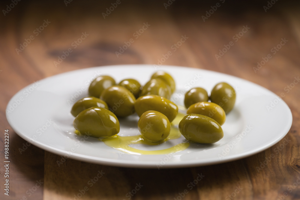 big green salted olives on white plate on wooden table big green salted olives on white plate on wooden table