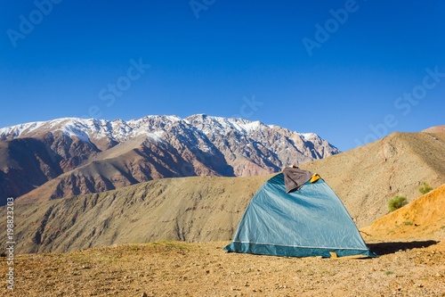 Igloo green camping tent on arid ground with splendid views of Andes snowy mountain range on the background under blue sky in Elqui Valley, Chile