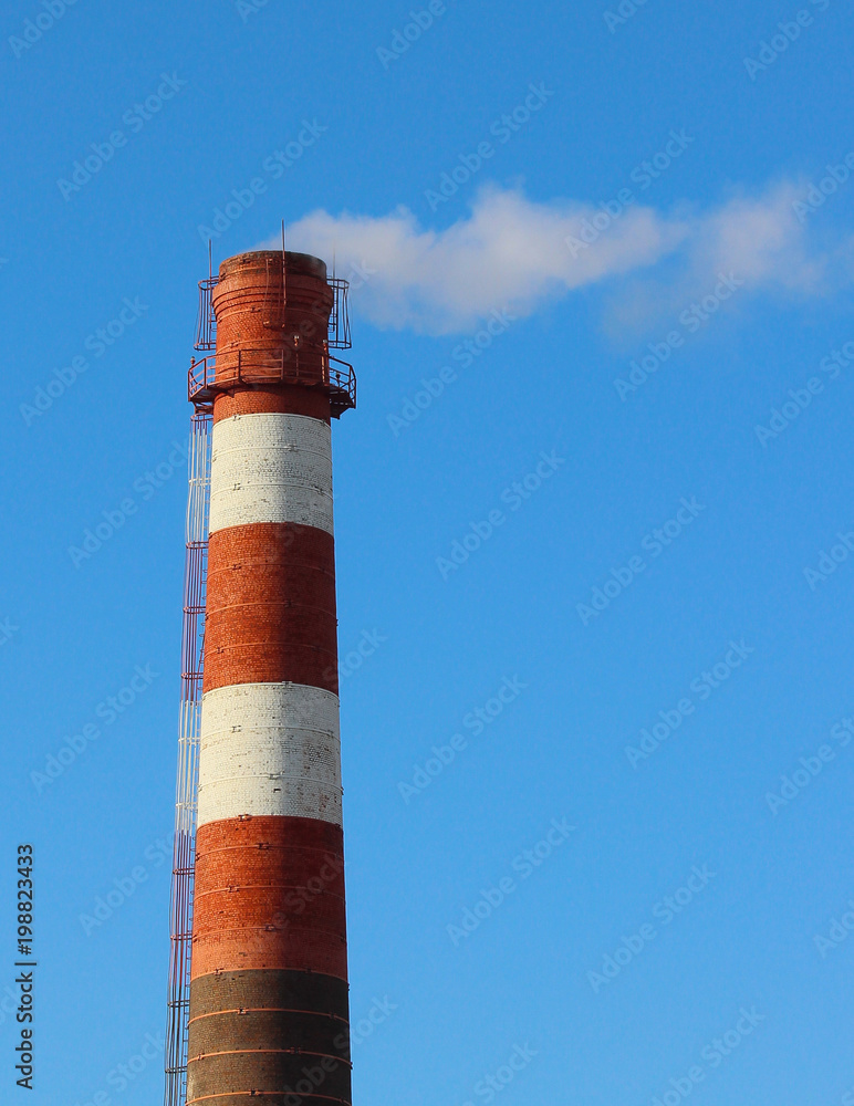 White smoke from a high brick industrial plant chimney against a blue sky White smoke from a high brick industrial plant chimney against a blue sky