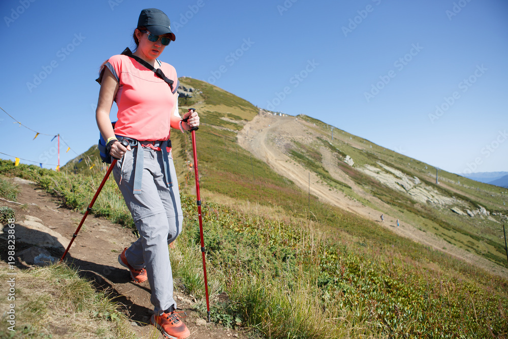 Photo of tourist girl walking with sticks and backpack on hill