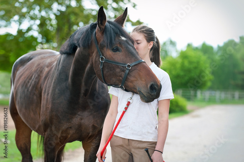 Young teenage girl tenderly kissing her favorite brown horse