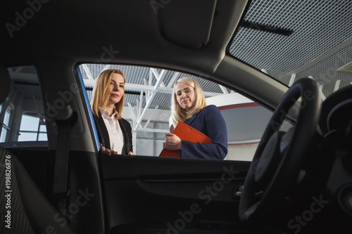 Visiting car dealership. Handsome sales manager is smiling while beautiful client is signing papers © burdun