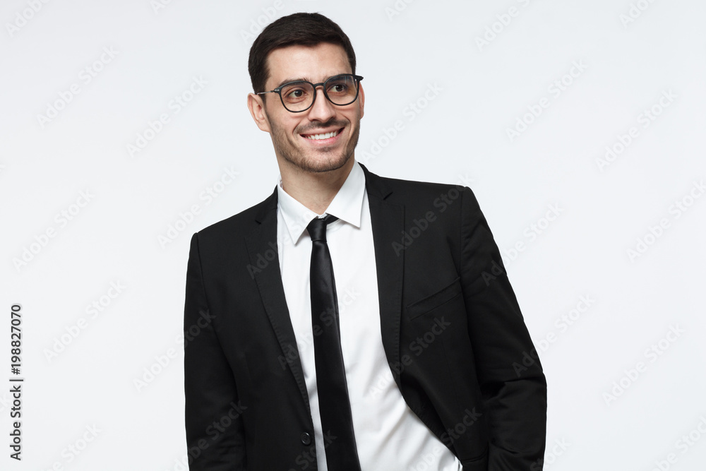 Modern business man in black suit looking away while standing in studio, isolated on grey background Modern business man in black suit looking away while standing in studio, isolated on grey background