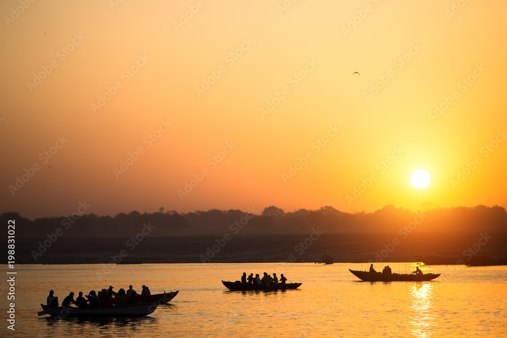 Naklejka premium Boat silhouettes with pilgrims during amazing sunset on the Holy Ganges river, Varanasi, India.