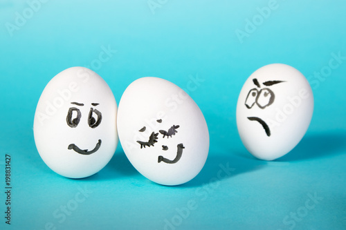 the hen eggs with painted faces. The dissatisfied man looks at the happy couple. Jealousy. Blue background.