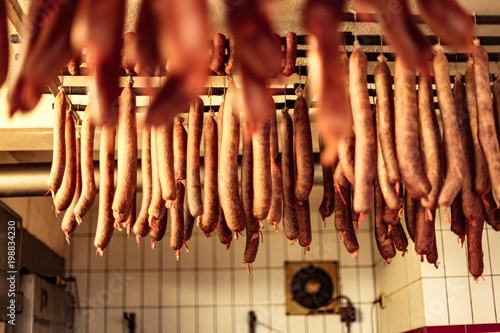 fresh handmade smoked sausages hanging in a white tile smokehouse of a butcher store